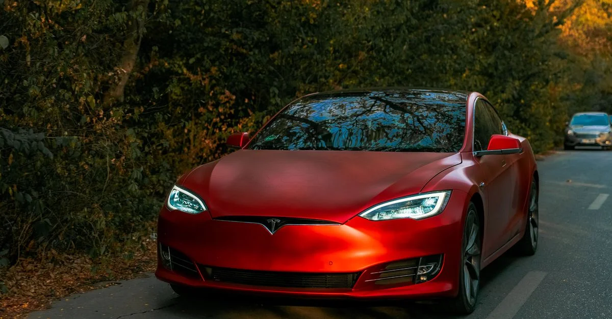 Voiture électrique rouge élégante roulant sur une route forestière pittoresque en automne.