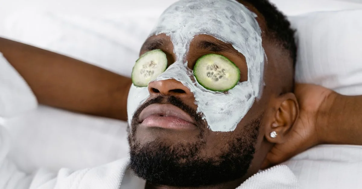 Un homme profitant d'une journée de soins personnels avec un masque facial et des tranches de concombre pour se détendre.